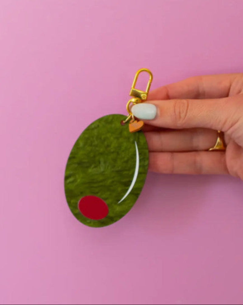 Hand holding a green oval keychain with a red dot on a pink background