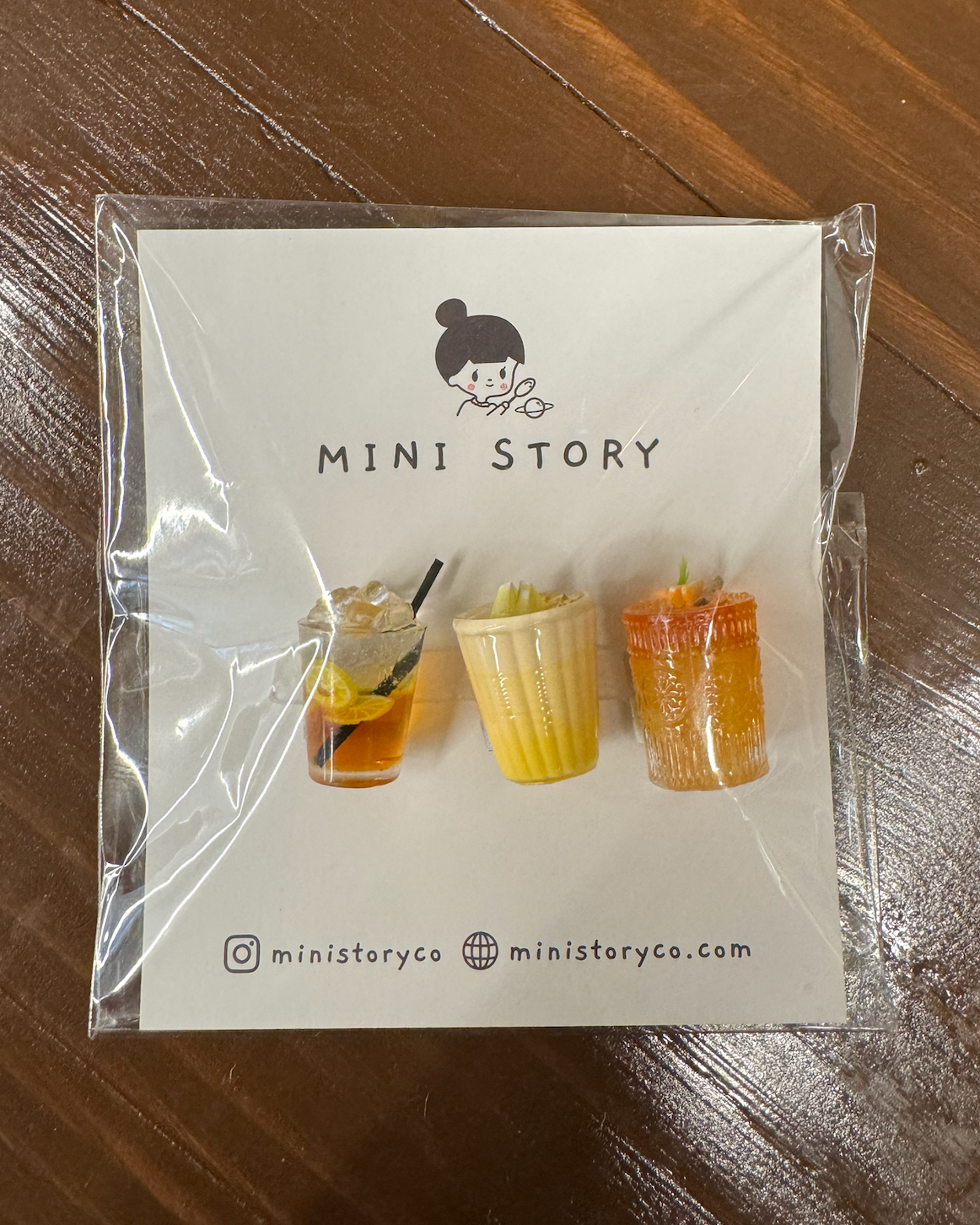 Packaging of 'MINI STORY' with illustrations of drinks on a wooden surface
