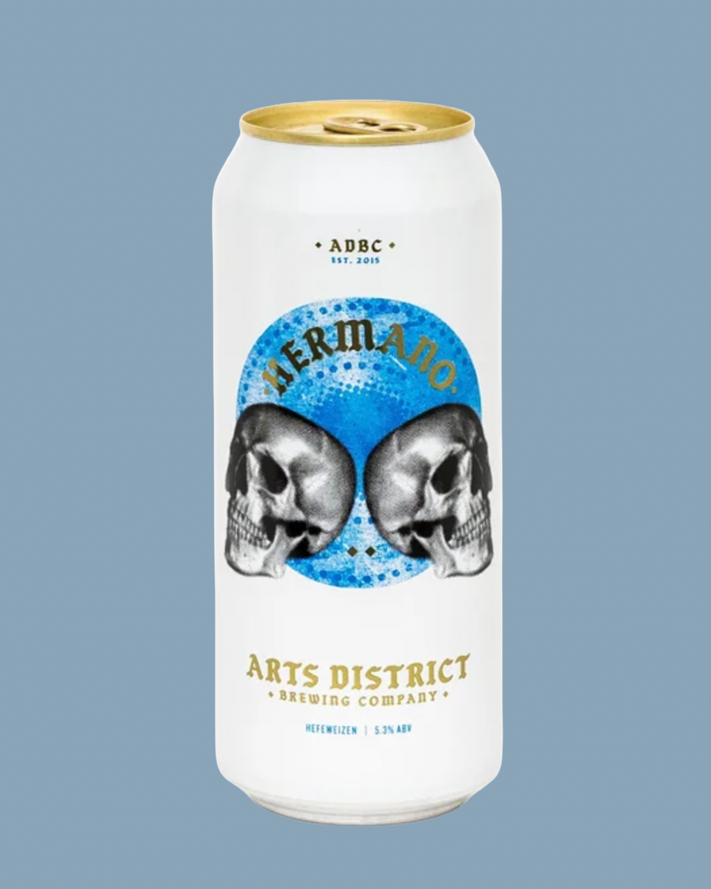 A white aluminum beer can with a gold pull tab and gold text, featuring a blue circular graphic with two black-and-white skulls and the word “Hermano.” The can is centered on a muted blue-gray background.