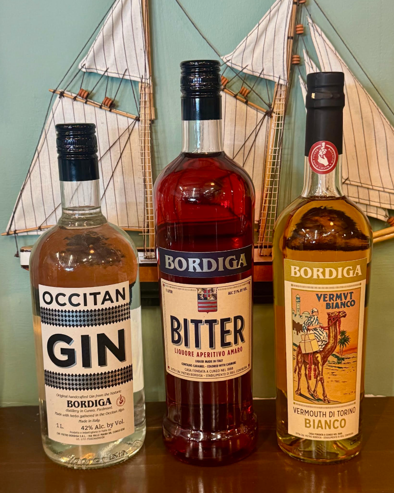 Three bottles of Bordiga spirits on a wooden surface with a ship model in the background.