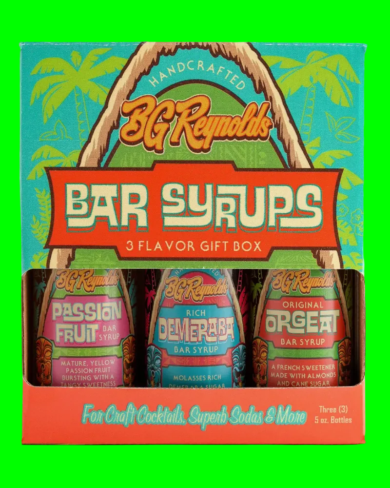 A 3-flavor gift box of 3G Reynolds Bar Syrups, featuring bottles of Passion Fruit, Delicate Rice, and Orgel bar syrup in a tropical-themed box with palm trees and a thatched arch.
