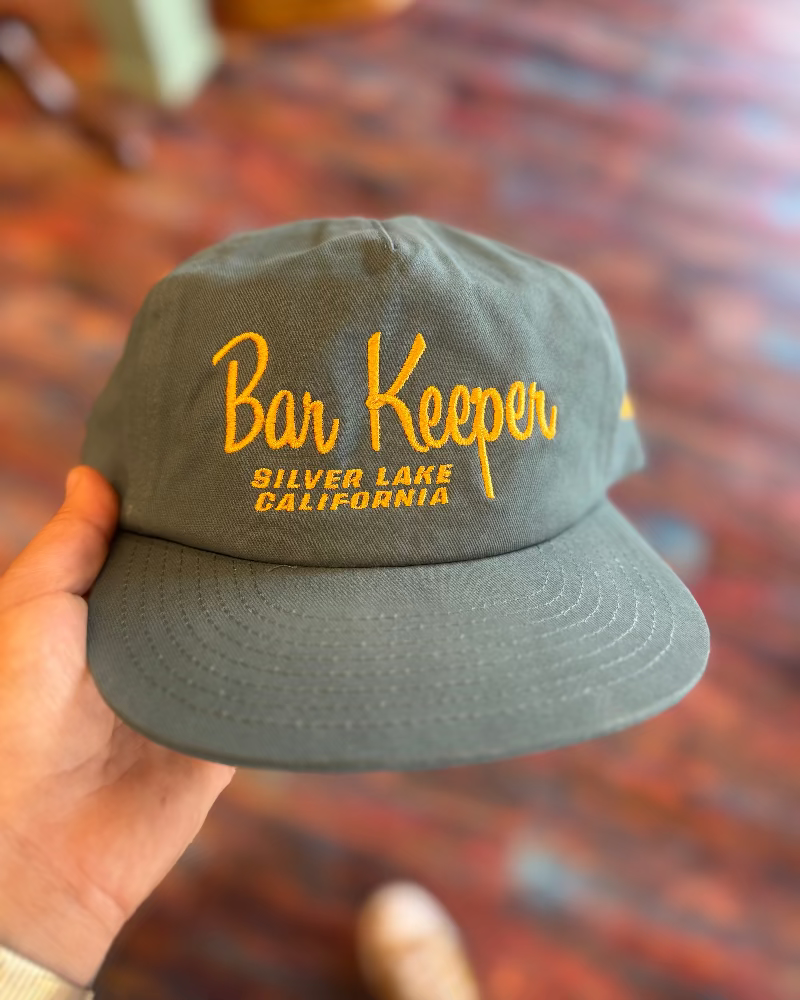 Gray cap with 'Bar Keeper Silver Lake California' text held by a hand on a blurred background