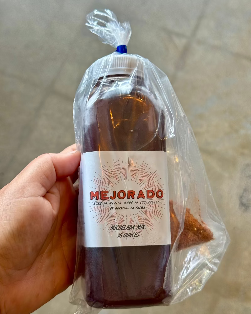 Hand holding a bottle of Mejorado Michelada Mix with a clear plastic bag.