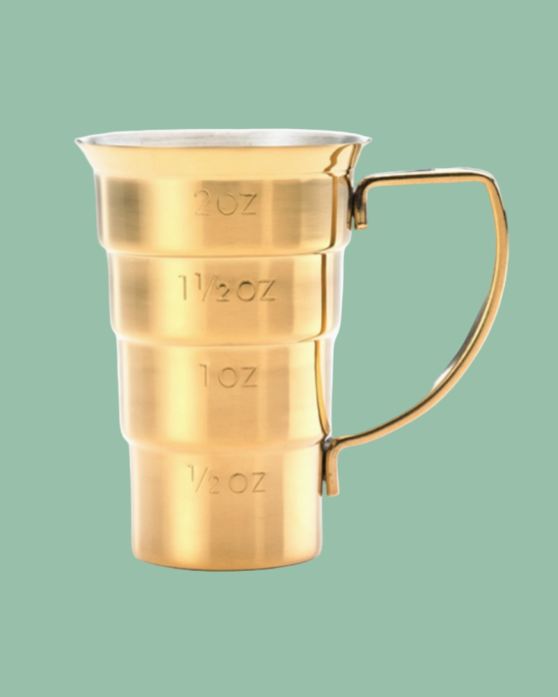 Gold measuring cup with ounces markings on a green background