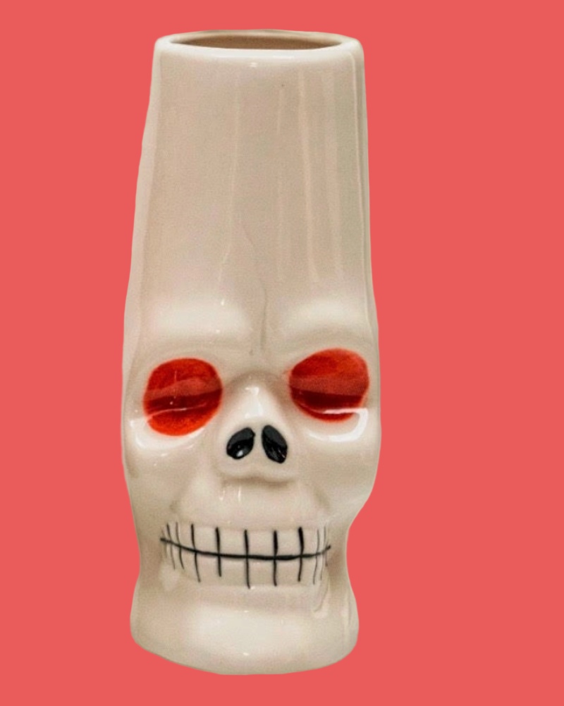 Skull-shaped mug with red eyes and a black mouth on a pink background