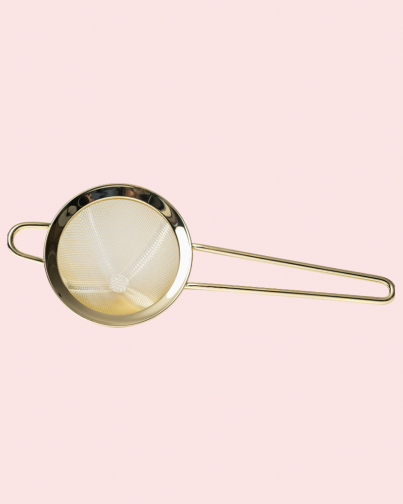 Gold strainer on a pink background