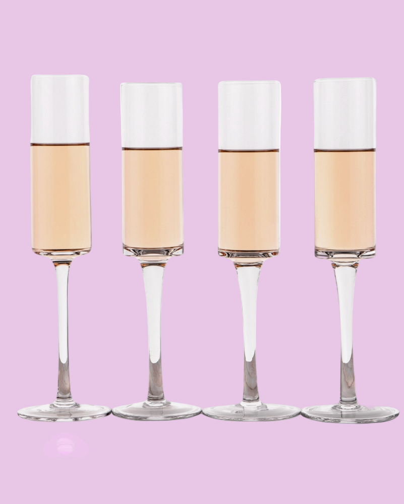 Four champagne flutes with white foam on a pink background