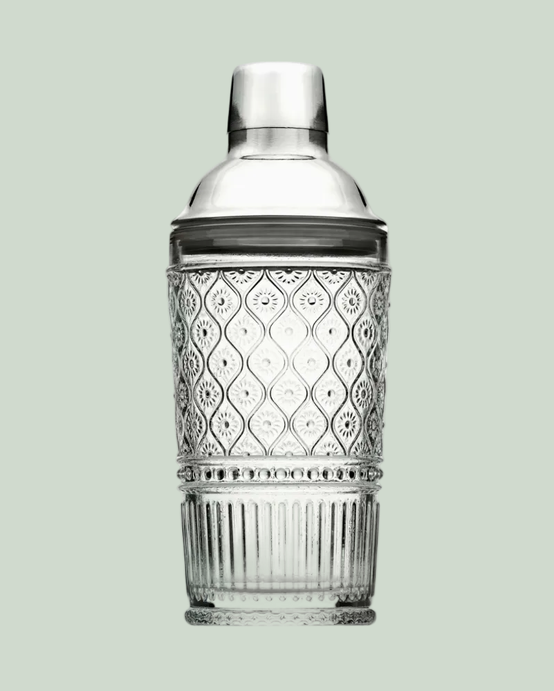 Decorative cocktail shaker with silver top and clear glass body on a light green background