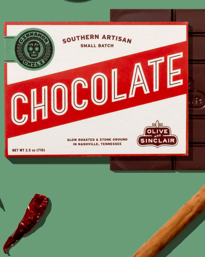 Box of Olive Sinclair Southern Artisan Chocolate with a cinnamon stick and red pepper on a green background