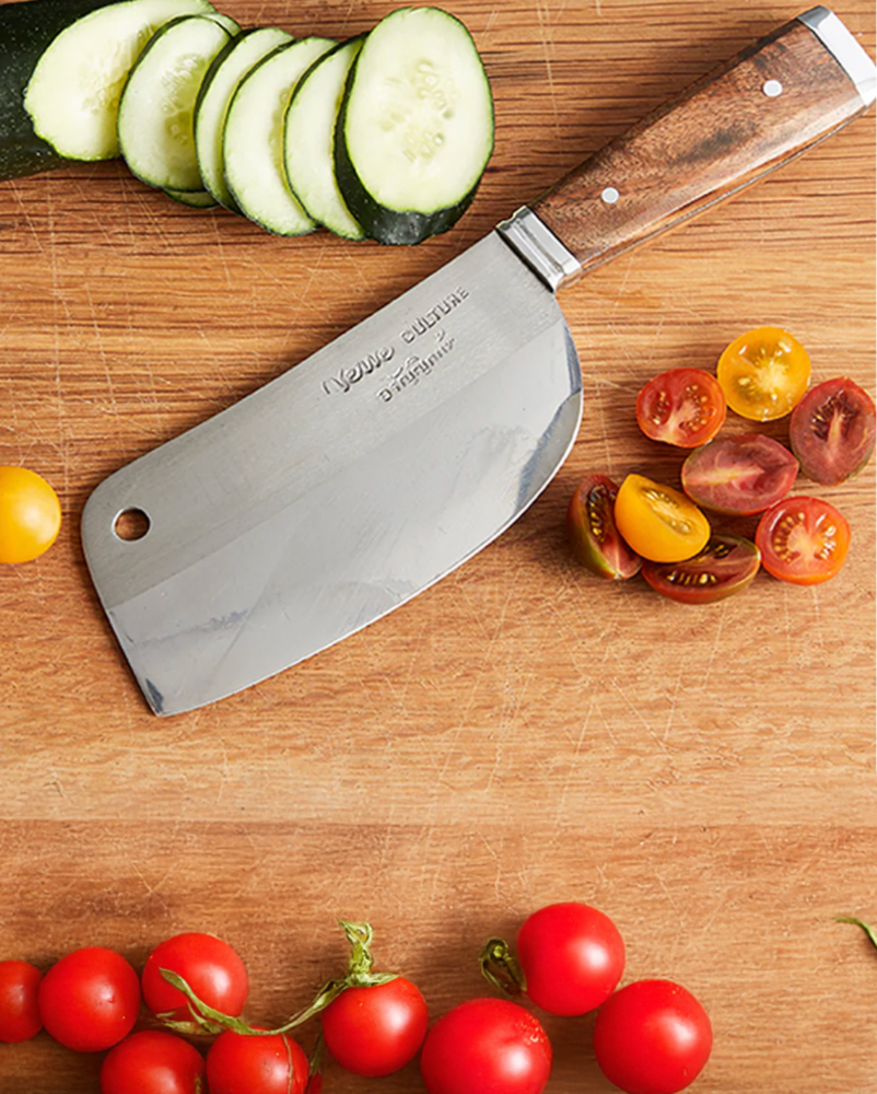 Knife with wooden handle on a cutting board surrounded by sliced cucumbers and tomatoes
