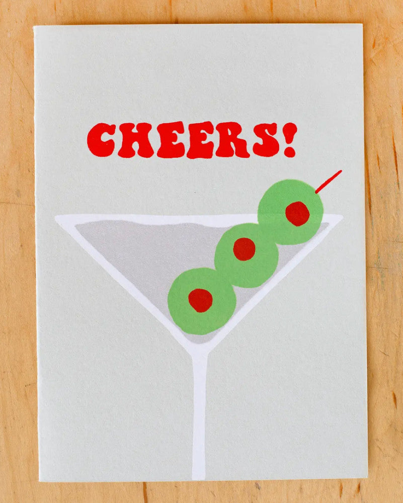 Card with 'Cheers!' text and martini glass design on a wooden surface