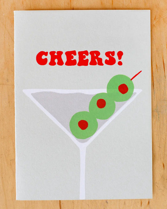 Card with 'Cheers!' text and martini glass design on a wooden surface