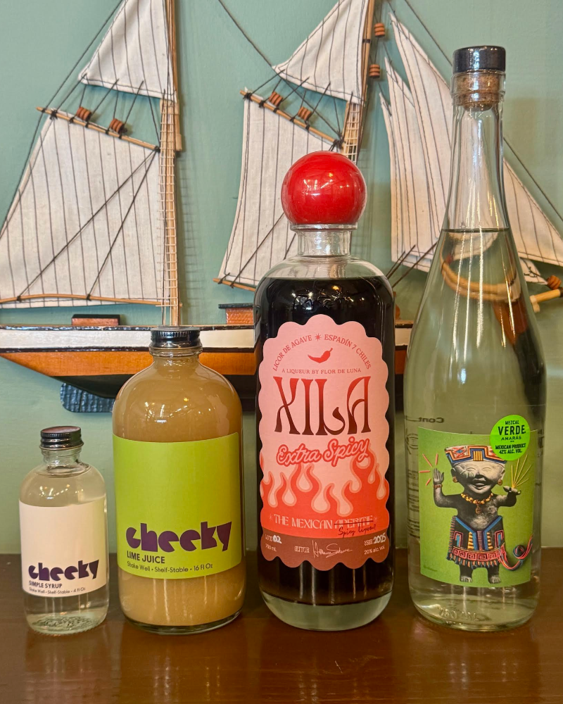 Four bottles of different types of drinks on a table with a sailboat decoration in the background.