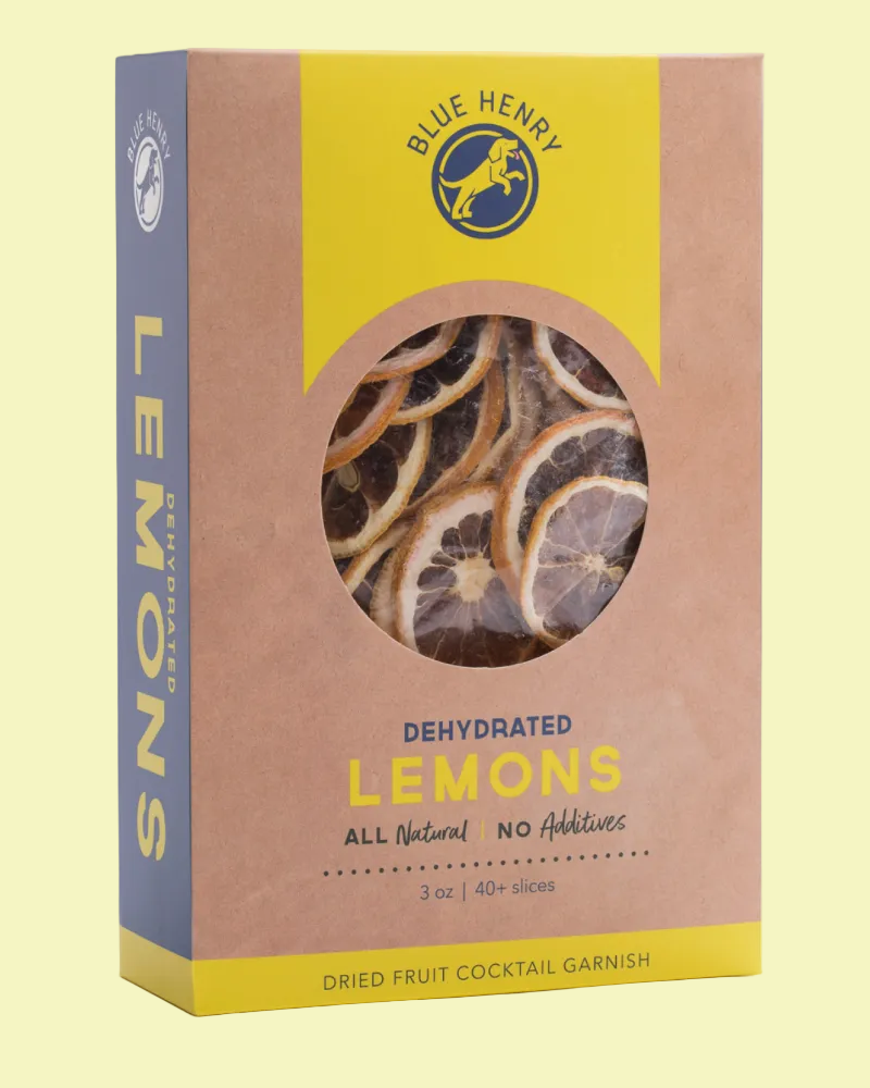 Blue Henry Dehydrated Lemons cocktail garnish in a kraft paper box with a yellow and blue design, featuring a circular window showing dried lemon slices inside.