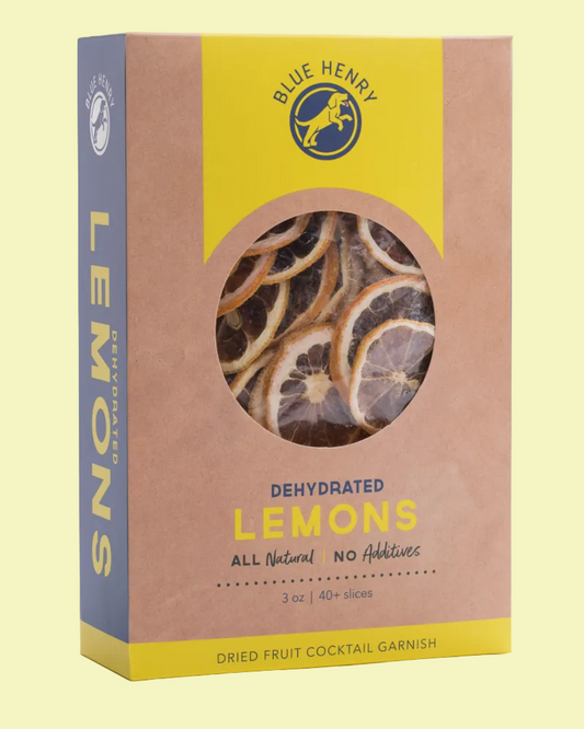 Blue Henry Dehydrated Lemons cocktail garnish in a kraft paper box with a yellow and blue design, featuring a circular window showing dried lemon slices inside.