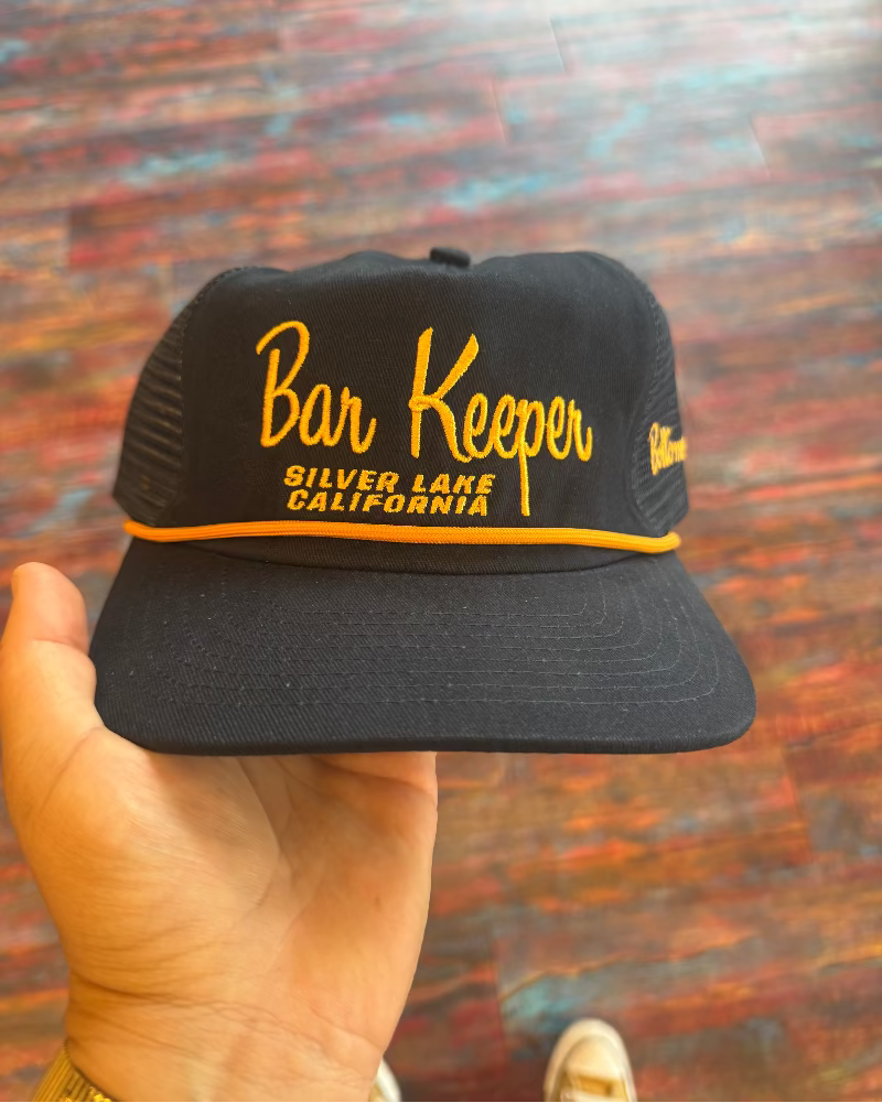 Black cap with 'Bar Keeper Silver Lake California' text held against a colorful background