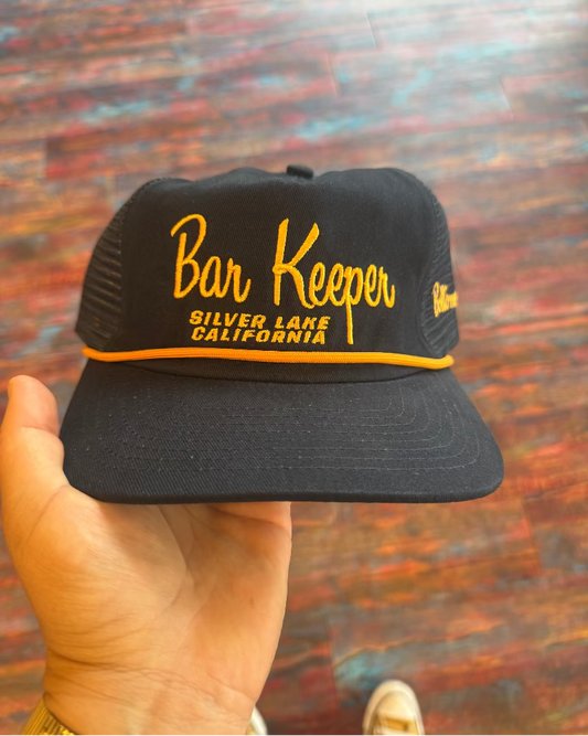 Black cap with 'Bar Keeper Silver Lake California' text held against a colorful background