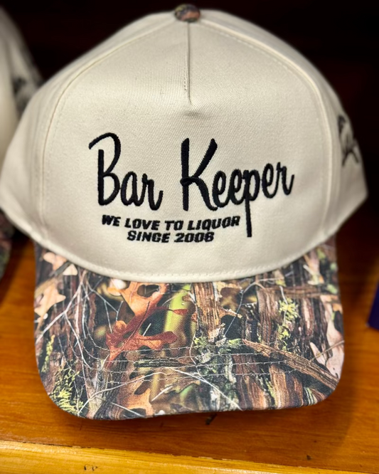 Cap with 'Bar Keeper' text and camouflage pattern on a wooden surface