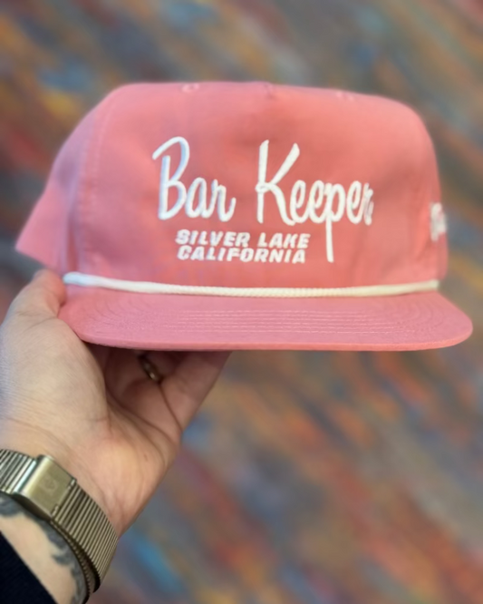 Pink cap with 'Bar Keeper Silver Lake California' text held by a hand against a colorful background
