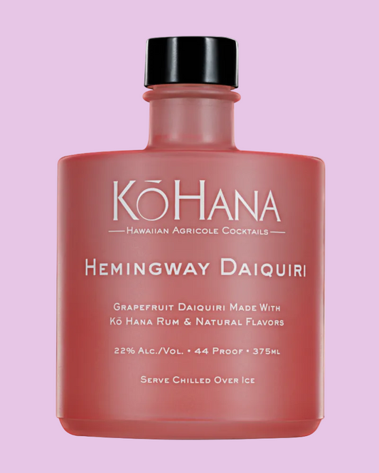 A bottle of Kó Hana Hemingway Daiquiri cocktail mix on a solid light purple background. The bottle is a dusty rose pink with a black cap, and the brand name 'Kó HANA' is printed in white on the front.