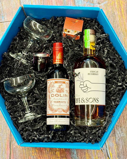 Two bottles of alcohol, a glass, and a small box in a blue box on a wooden surface.