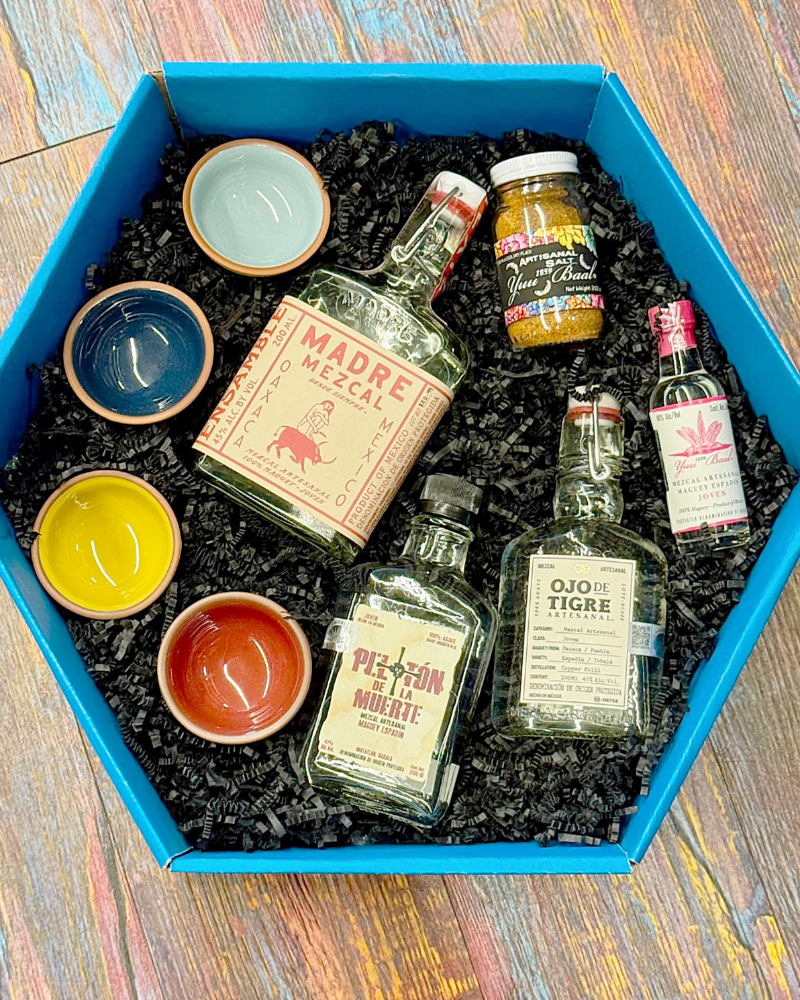 Collection of tequila bottles and small bowls in a blue box on a wooden surface