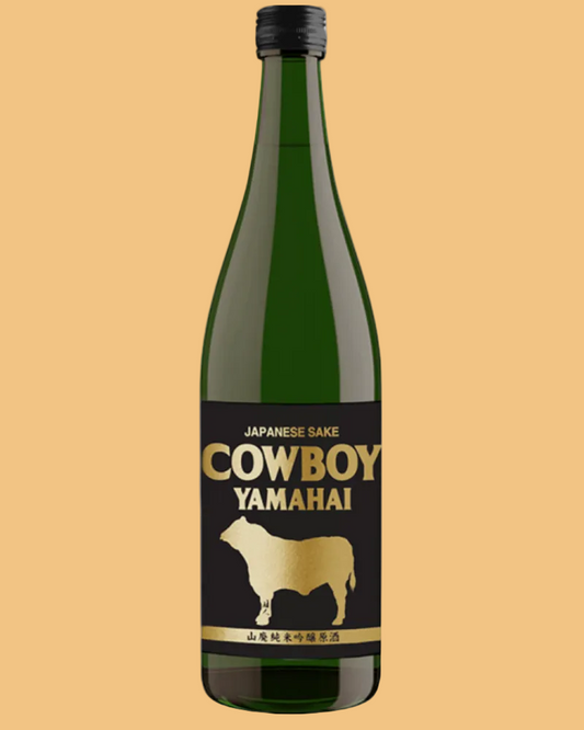 A bottle of Yamaha Cowboy Japanese Sake on a plain white background. The bottle is dark green glass with a black cap and a black label featuring gold lettering and a gold silhouette of a cow.