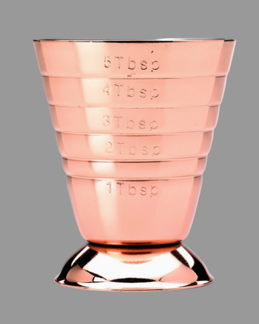 Rose gold measuring cup with embossed measurements on a gray background