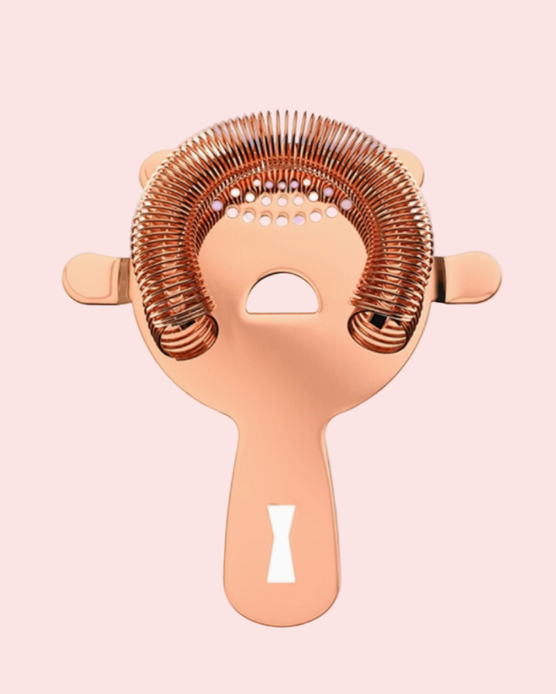 Rose gold cocktail strainer on a light pink background