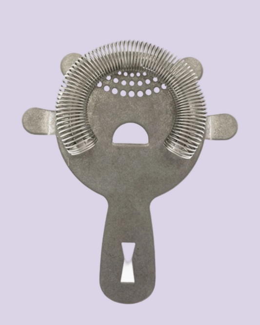 Metallic cocktail strainer on a light purple background
