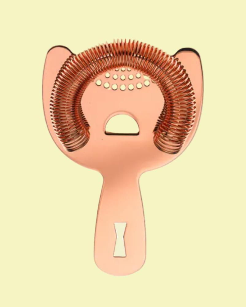 Rose gold cocktail strainer on a light yellow background
