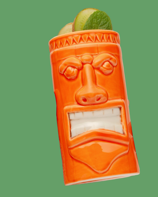 Orange tiki mug with a face design filled with apples and a lime on a green background