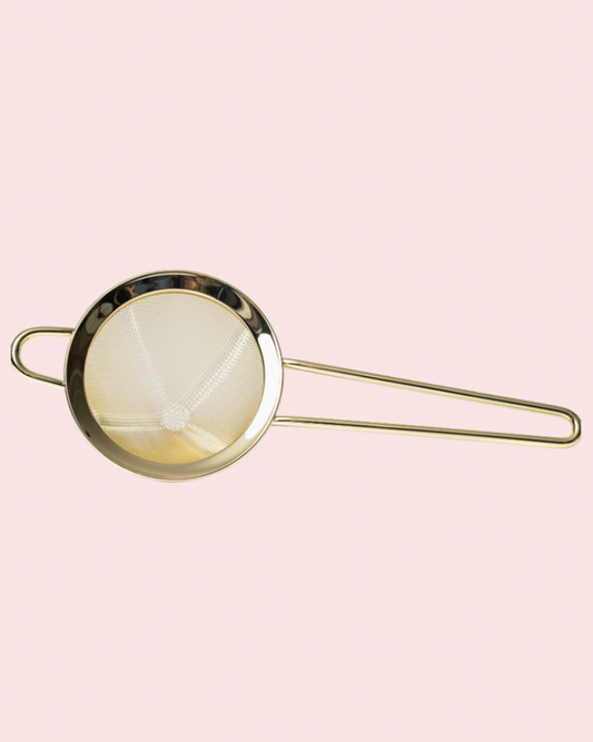 Gold strainer on a pink background
