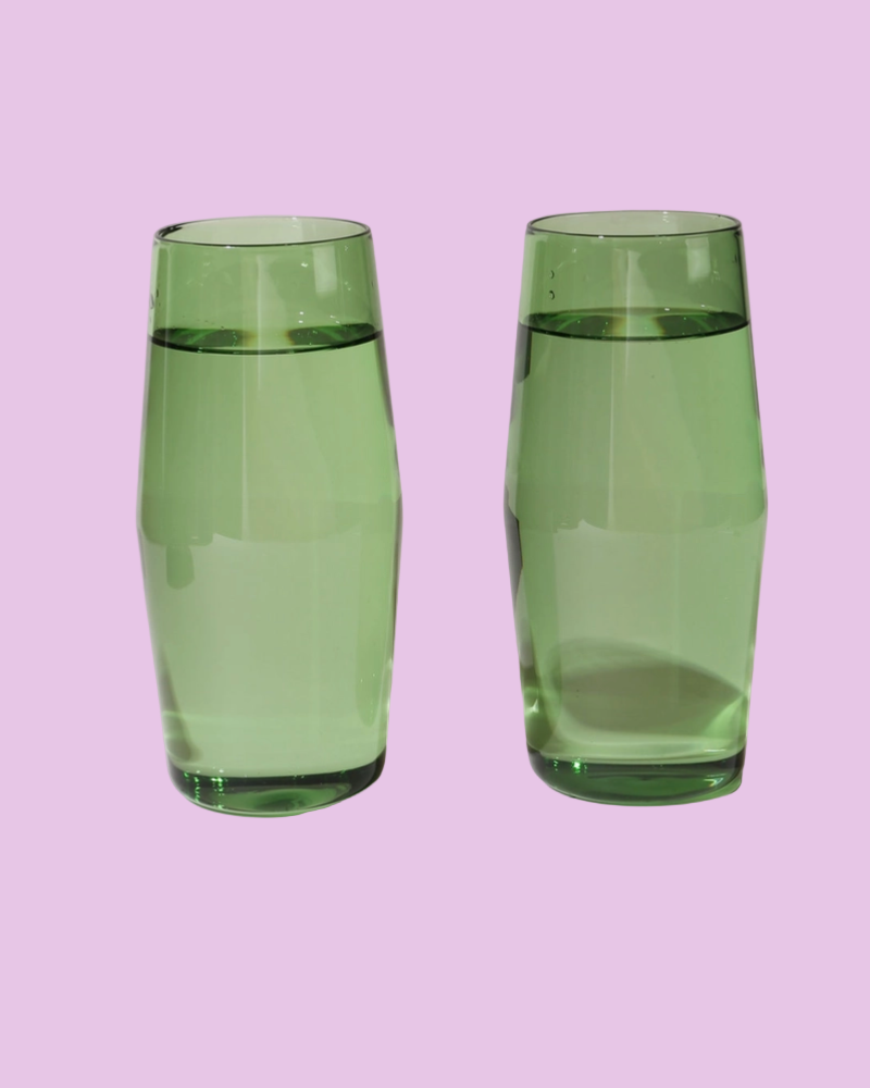 Two green glass tumblers filled with water on a pink background