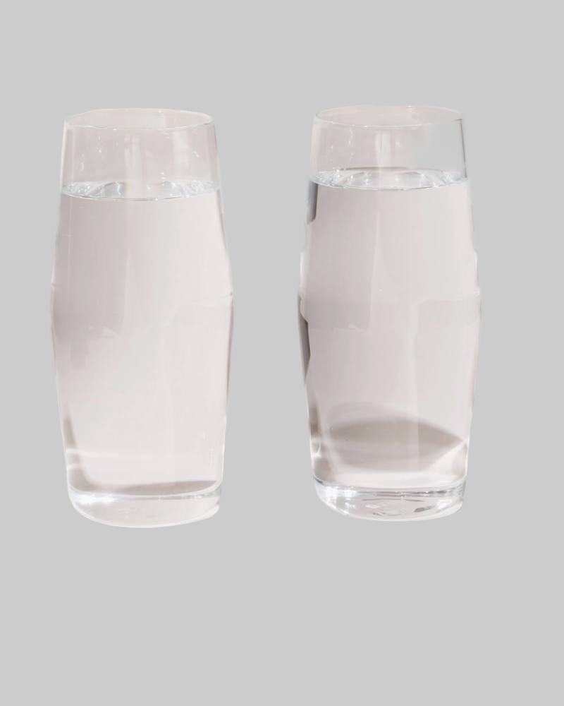 Two clear glass tumblers filled with water on a gray background