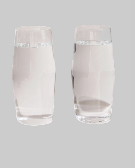 Two clear glass tumblers filled with water on a gray background