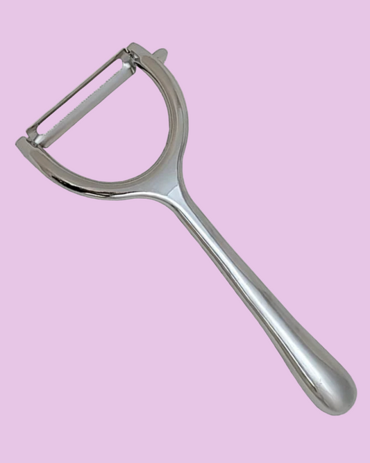 Metallic vegetable peeler on a pink background