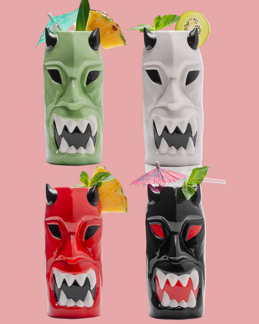 Four mask-shaped tumblers with tropical drinks on a pink background