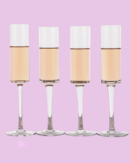 Four champagne flutes with white foam on a pink background