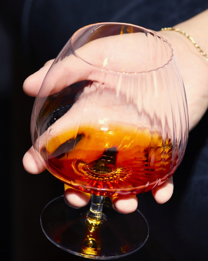 Hand holding a glass of amber liquid against a dark background