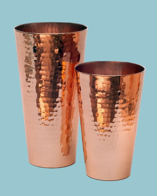 Two copper tumblers with a hammered texture on a light blue background