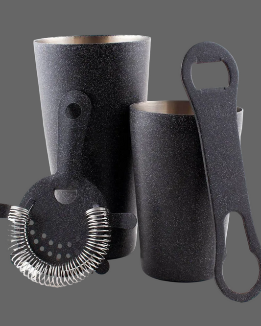 Set of black textured bar tools including a jigger, bottle opener, and strainer on a gray background.