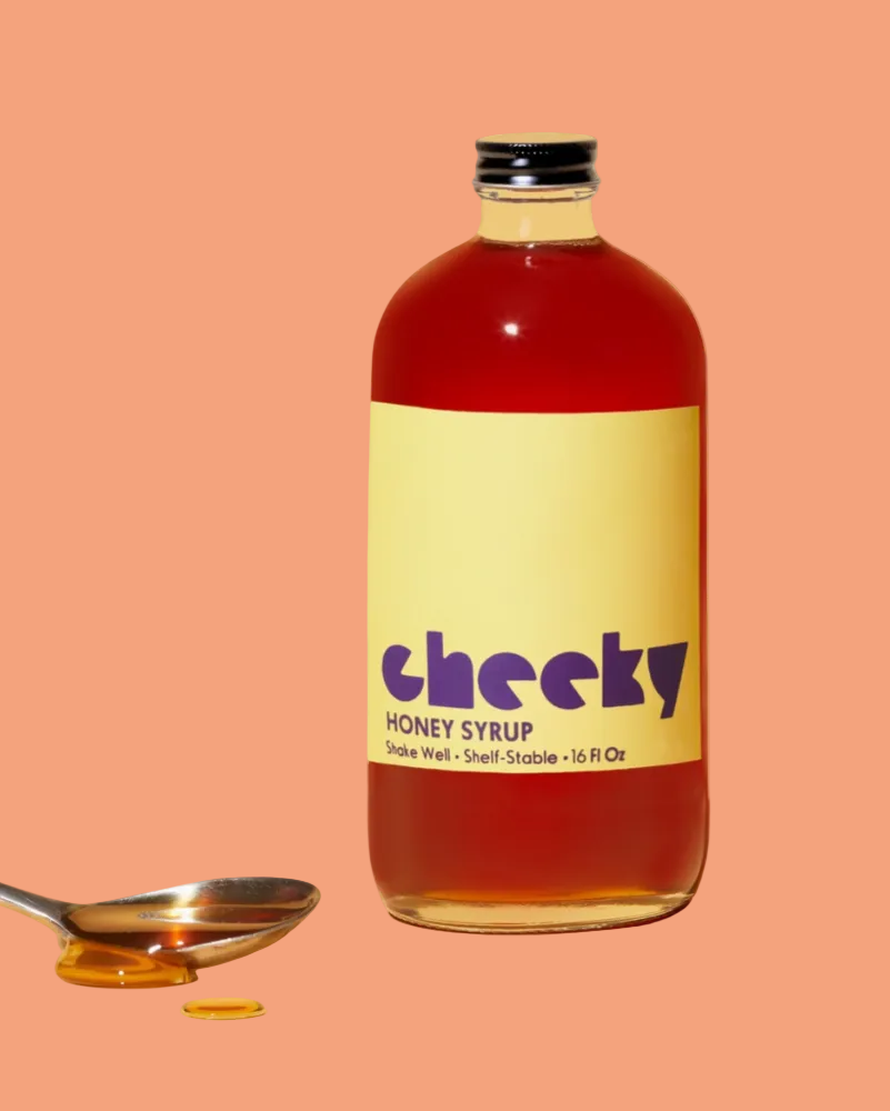 Bottle of Cheeky honey syrup with a spoonful of syrup on a peach background
