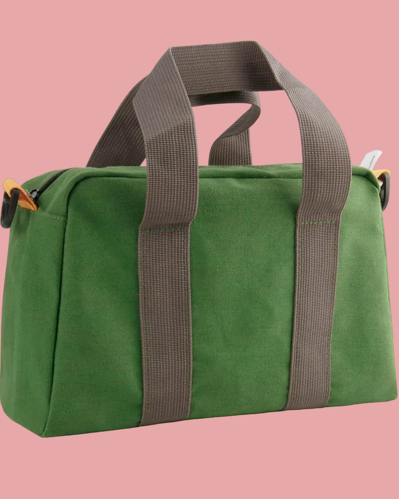 Green duffel bag with brown straps on a pink background