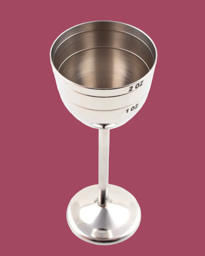 Silver measuring cup with markings on a pink background