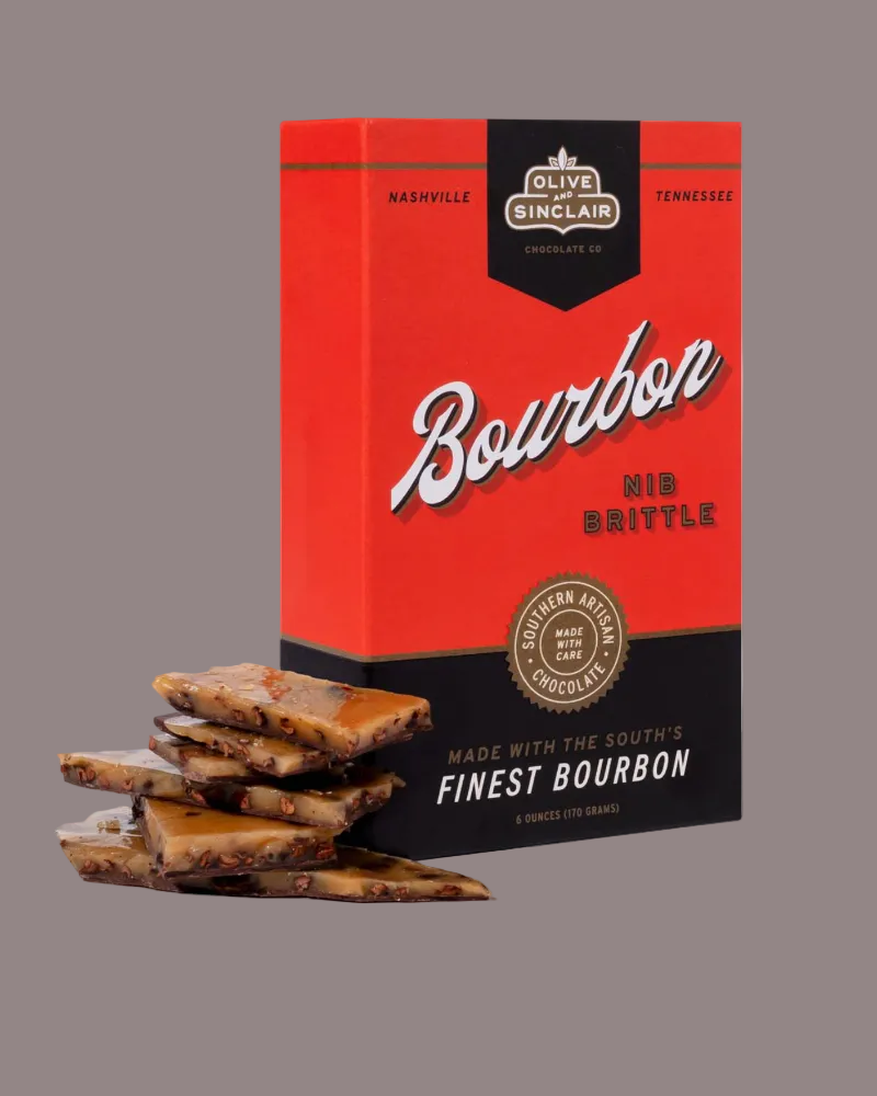 Box of Olive & Sinclair Bourbon Brittle with brittle pieces in front on a white background