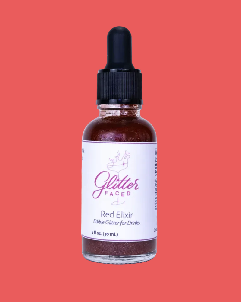 Bottle of Glitter Faced Red Elixir on a coral background