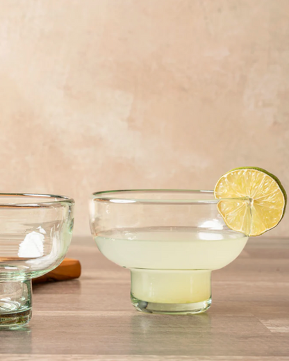 Two glass bowls with a lime wedge on a wooden surface against a beige wall.