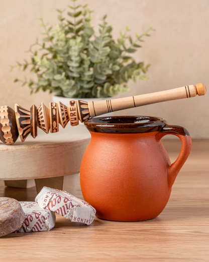 Two terracotta mugs, a bag labeled 'Villa Real', and a wooden pestle on a wooden surface with a plant in the background.
