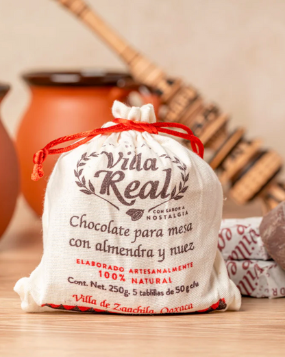 Villa Real chocolate packaging on a wooden surface with clay mugs and a stone in the background